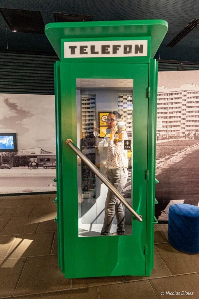 Femme utilisant une cabine téléphonique verte marquée "TELEFON" au Musée de l'Émigration de Gdynia.