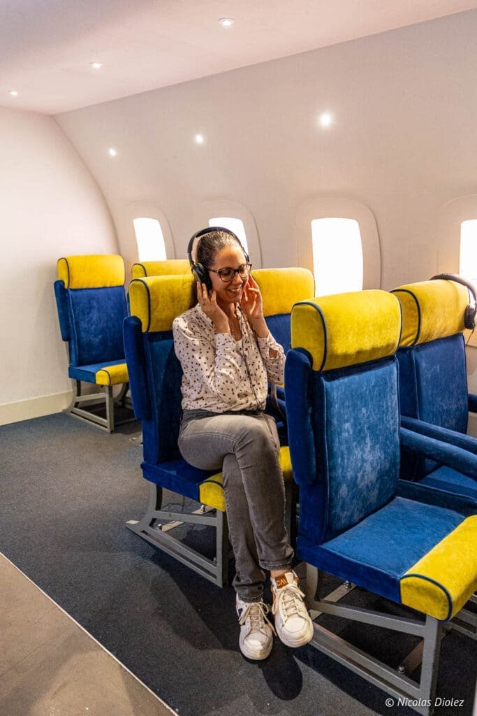 Femme souriante avec casque dans une reconstitution de cabine d'avion au Musée de la Migration Gdynia.