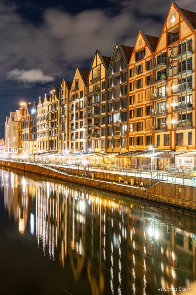 Façades illuminées de Gdańsk la nuit avec reflets sur la rivière Motława.
