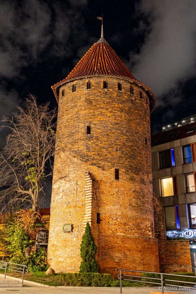Tour de la ville médiévale de Gdańsk en briques, éclairée la nuit.