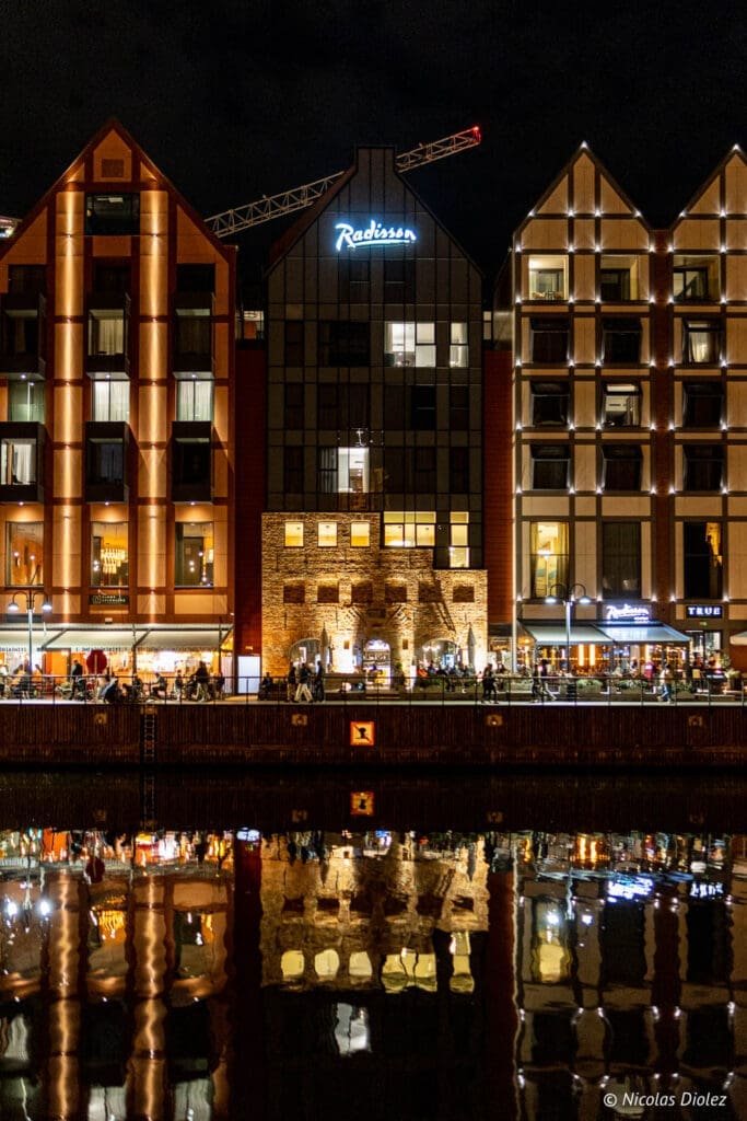Bâtiments illuminés de Gdańsk la nuit, avec hôtel Radisson et reflets sur l'eau.