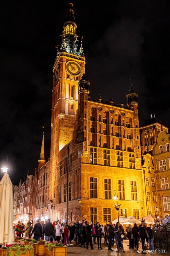 Hôtel de Ville de Gdańsk illuminé la nuit avec foule en contrebas.