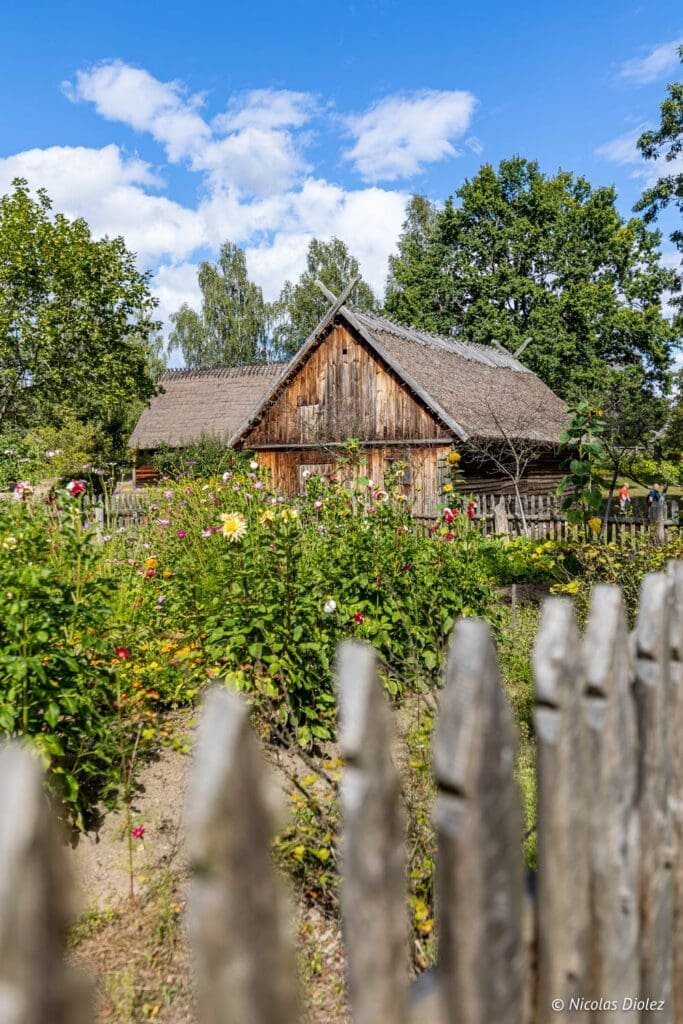 Ferme traditionnelle kaszubska avec toit de chaume et jardin fleuri en Poméranie.