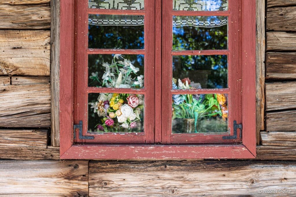 Fenêtre en bois rouge avec fleurs artificielles au Parc ethnographique de Kaszuby.