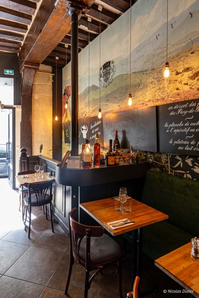 Sala del bistrot La Ferrandaise a Parigi, con il bancone, tavoli di legno e un affresco di montagna sulla parete.