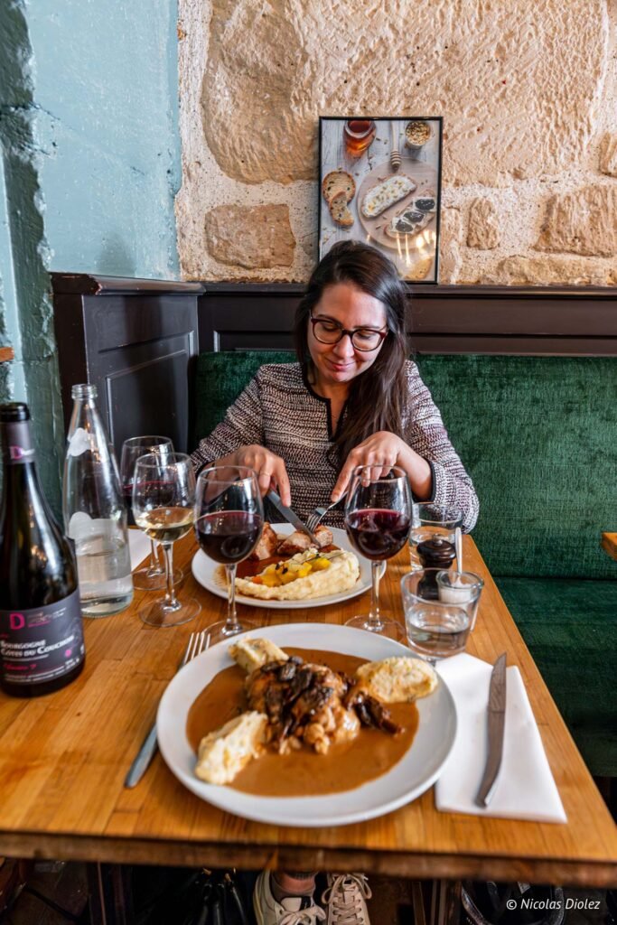 Gaëlle davanti al suo piatto nel bistrot La Ferrandaise a Parigi, con una bottiglia di vino rosso sul tavolo.