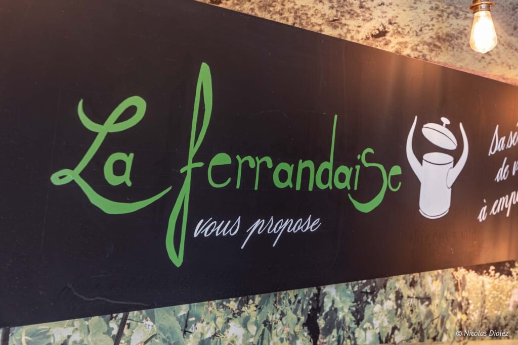 Lavagna « La Ferrandaise vous propose » sulla parete del bistrot, sotto un affresco di prato.