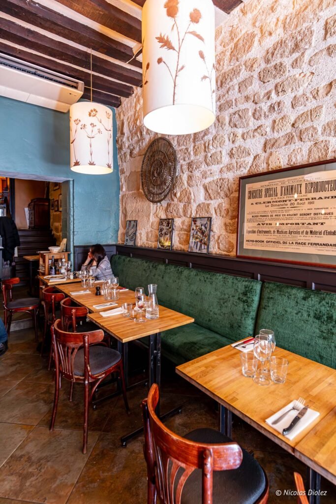 Sala de La Ferrandaise a Parigi, panche di velluto verde, sedie da bistrot e muro di pietra.