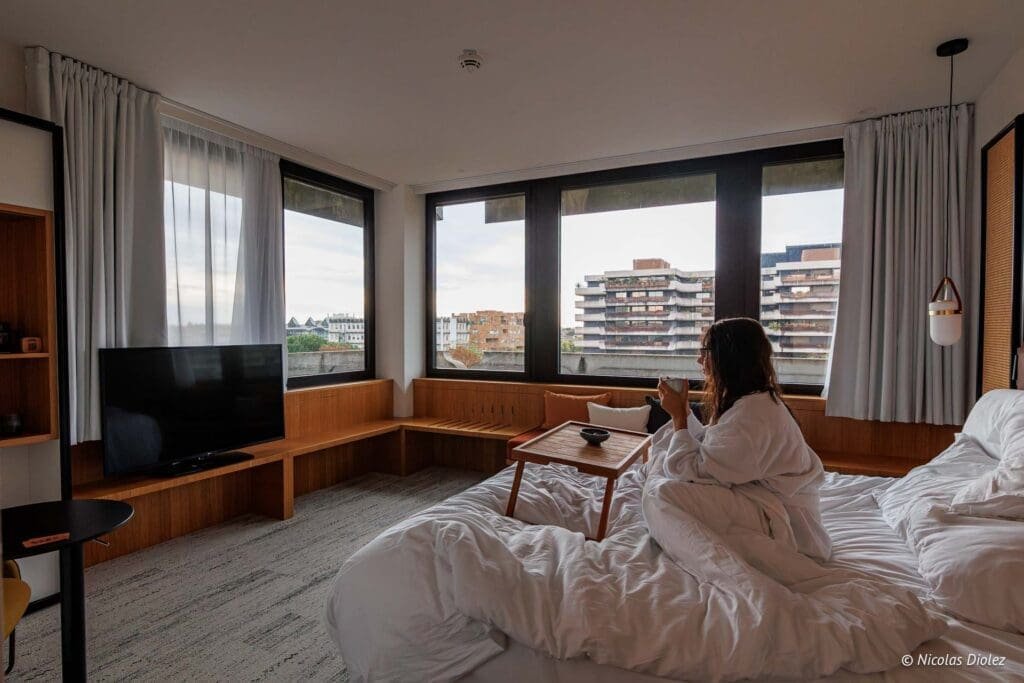 Femme en peignoir buvant une tasse dans une chambre d'hôtel lumineuse à Bordeaux.