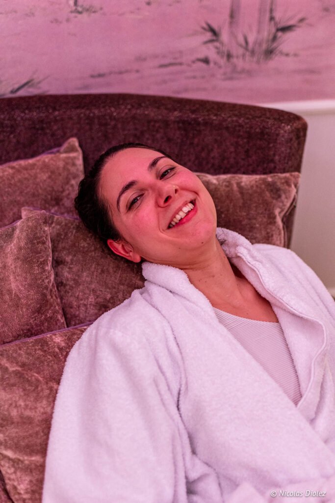 Donna sorridente in accappatoio bianco, sdraiata su una poltrona della spa.