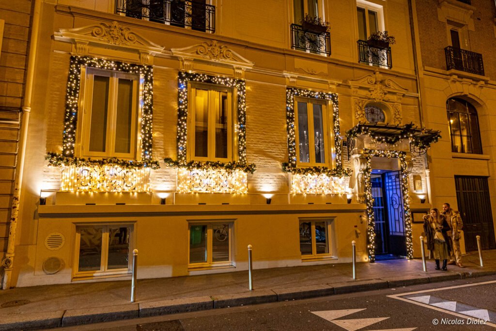 Facciata dell'hotel Paris j'Adore decorata con luci, rue Beudant, la sera.
