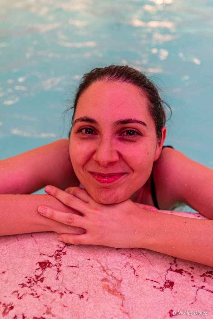 Donna sorridente appoggiata al bordo in marmo della piscina della spa.