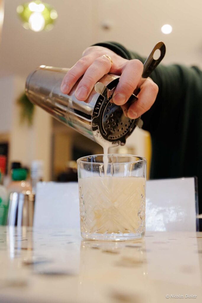 Versement d'un cocktail crémeux d'un shaker dans un verre taillé.