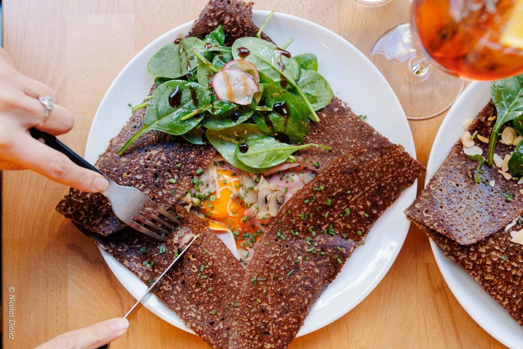 La creperie bretonne fleurie - DR Nicolas Diolez 2017 Découpe de galette sarrasin œuf jambon champignons et salade, main et couverts.