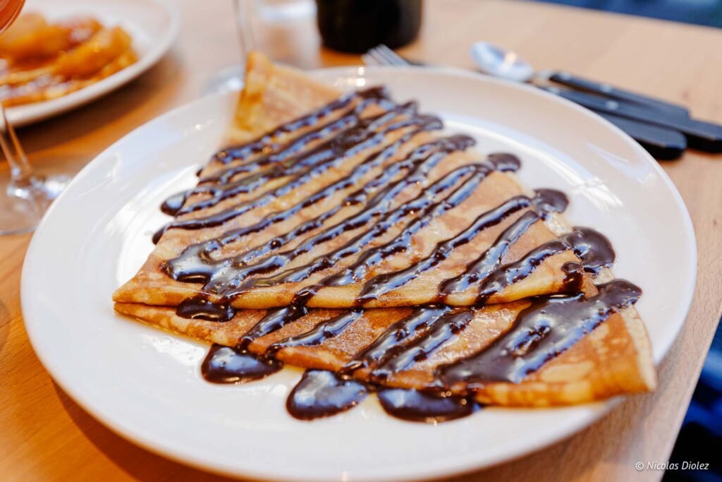 Crêpe pliée avec sauce au chocolat sur assiette blanche.