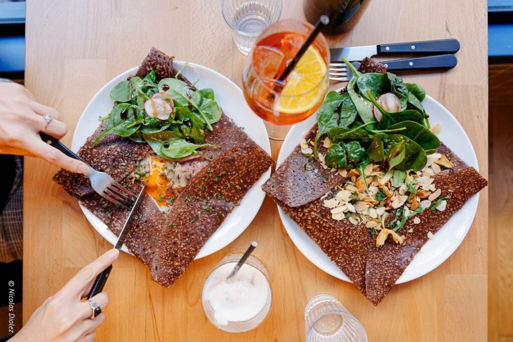 Deux galettes de sarrasin garnies de légumes, œuf, et amandes effilées, avec boissons.