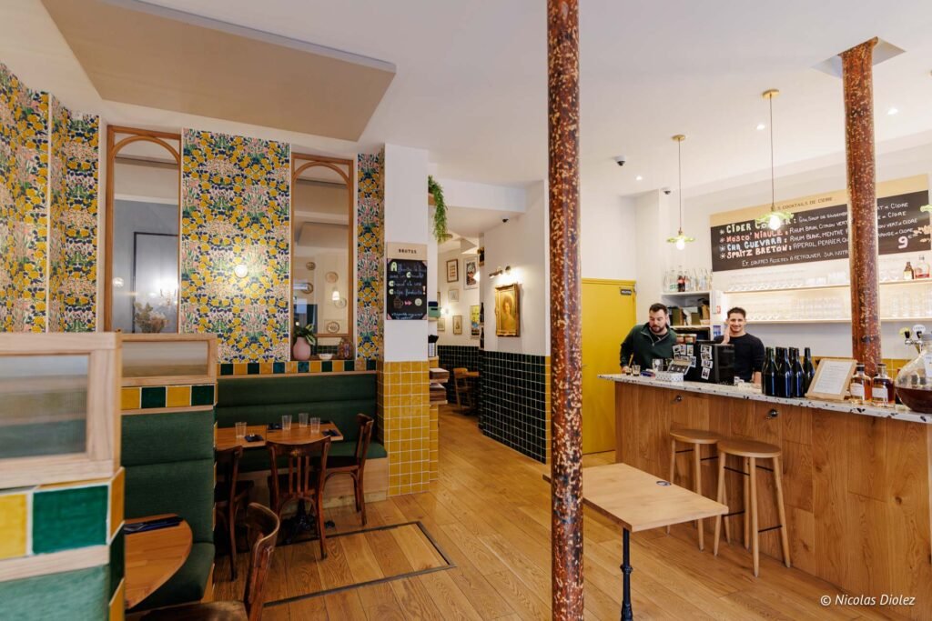 Intérieur du restaurant Brutus avec banquettes vertes, papier peint fleuri et bar en bois.