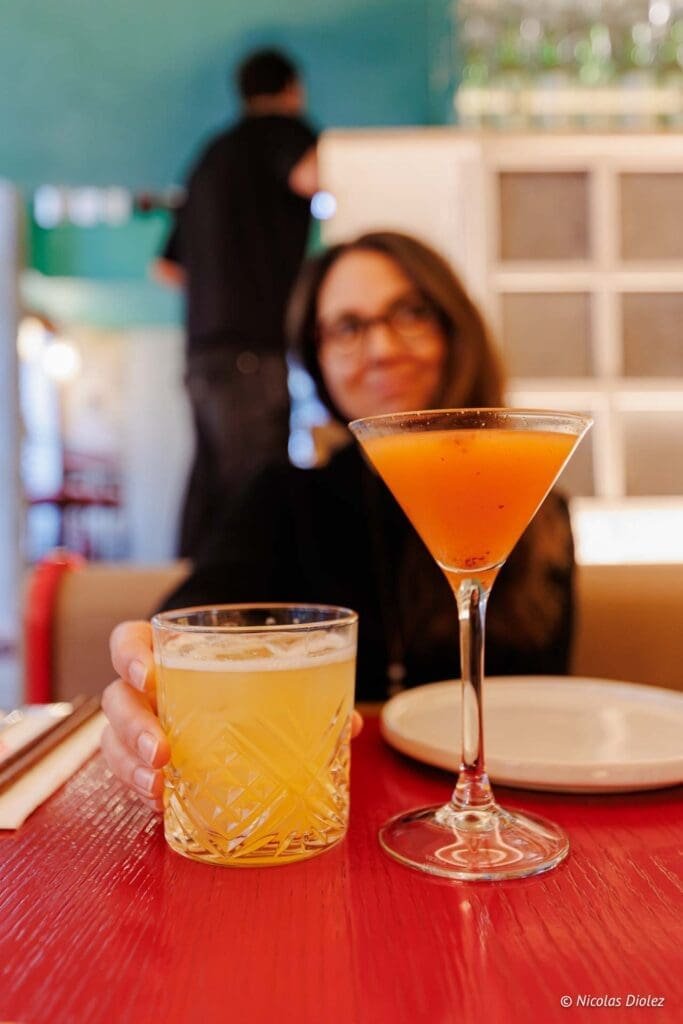 Cocktails Hallyu Kitchen : boisson orange et verre texturé sur table rouge.