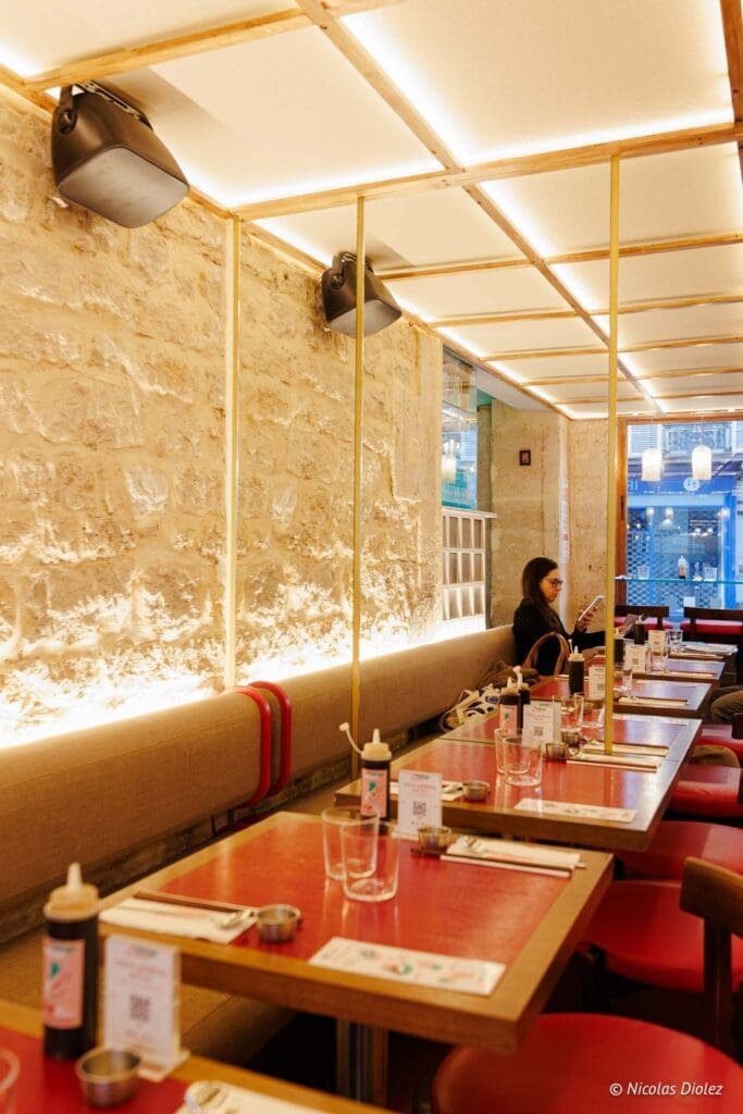 Intérieur restaurant coréen Hallyu Kitchen avec tables rouges et mur en pierre.