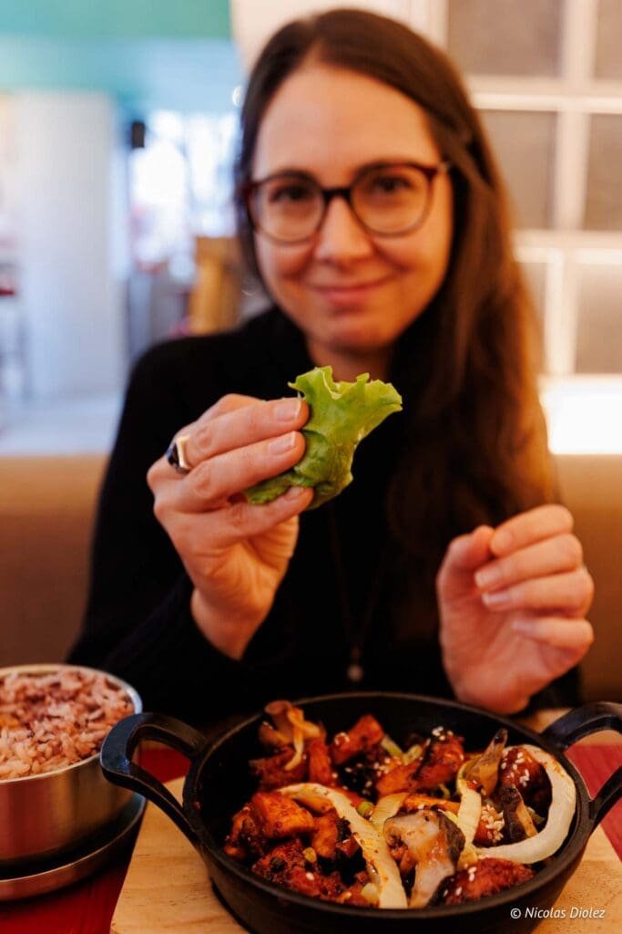 Femme souriante mangeant un plat coréen avec une feuille de laitue chez Hallyu Kitchen.