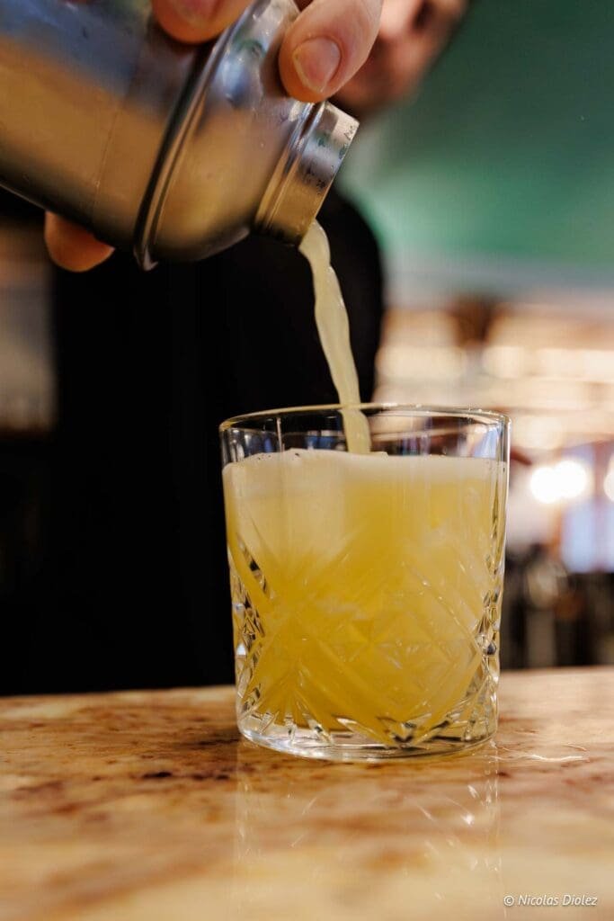 Préparation d'un cocktail jaune pétillant dans un verre à whisky texturé à Hallyu Kitchen.