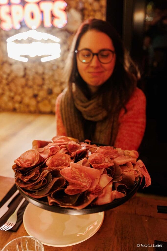 Assiette de charcuterie devant une femme souriante, enseigne néon "HOT SPOTS".