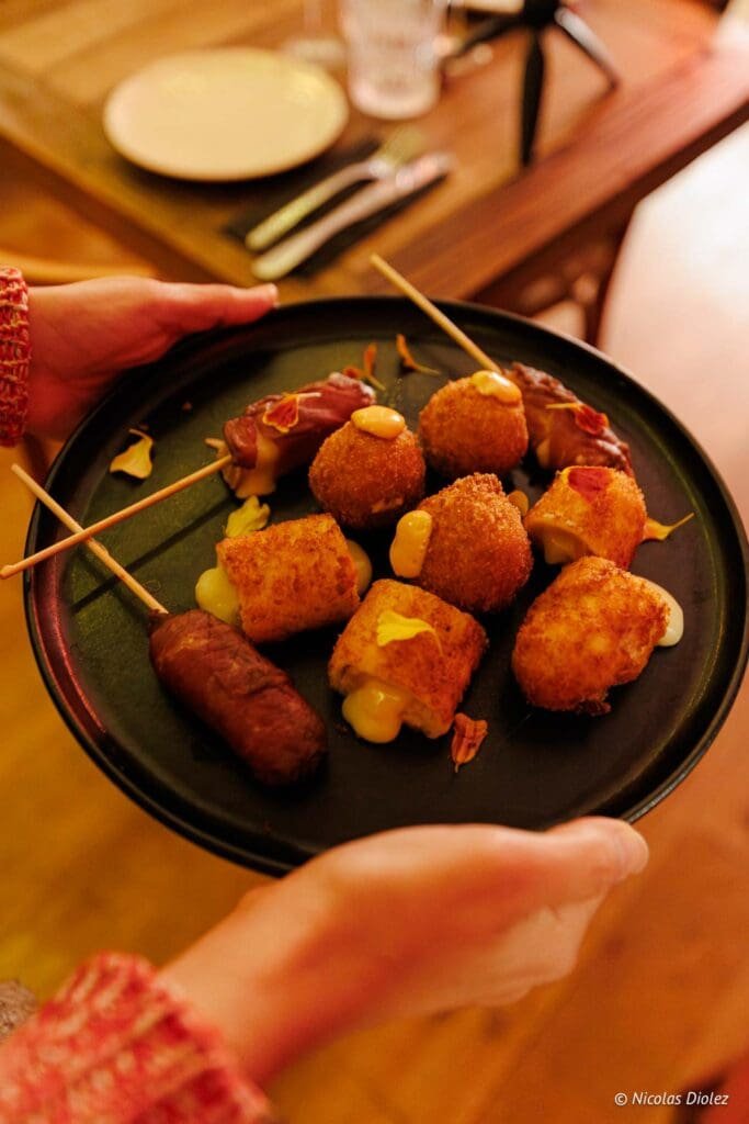 Assiette de tapas et amuse-gueules chauds avec fromage fondant, tenue par des mains.