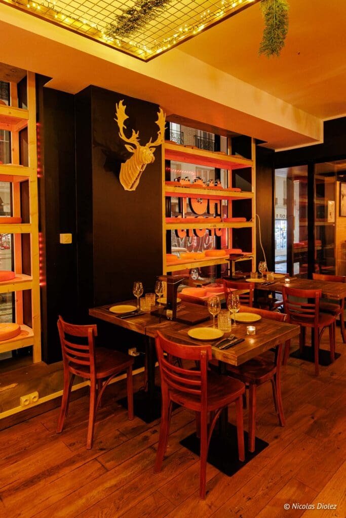 Intérieur restaurant ambiance bois avec tête de cerf décorative et étagères à fromages.