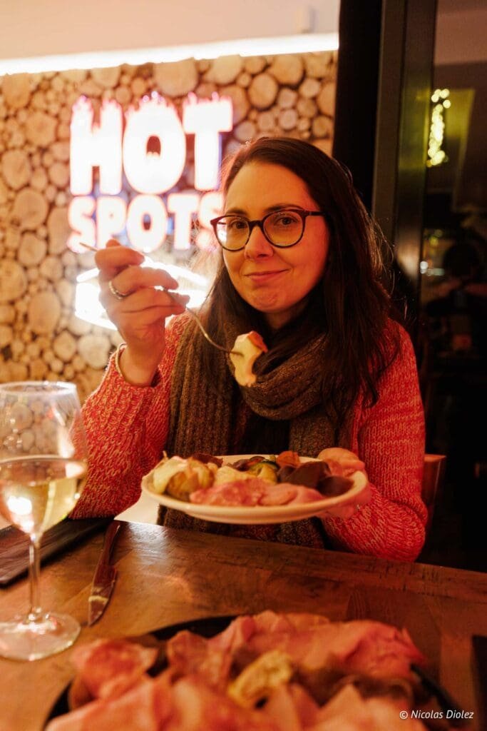 Femme mangeant charcuterie chez Hot Spots, verre de vin blanc.