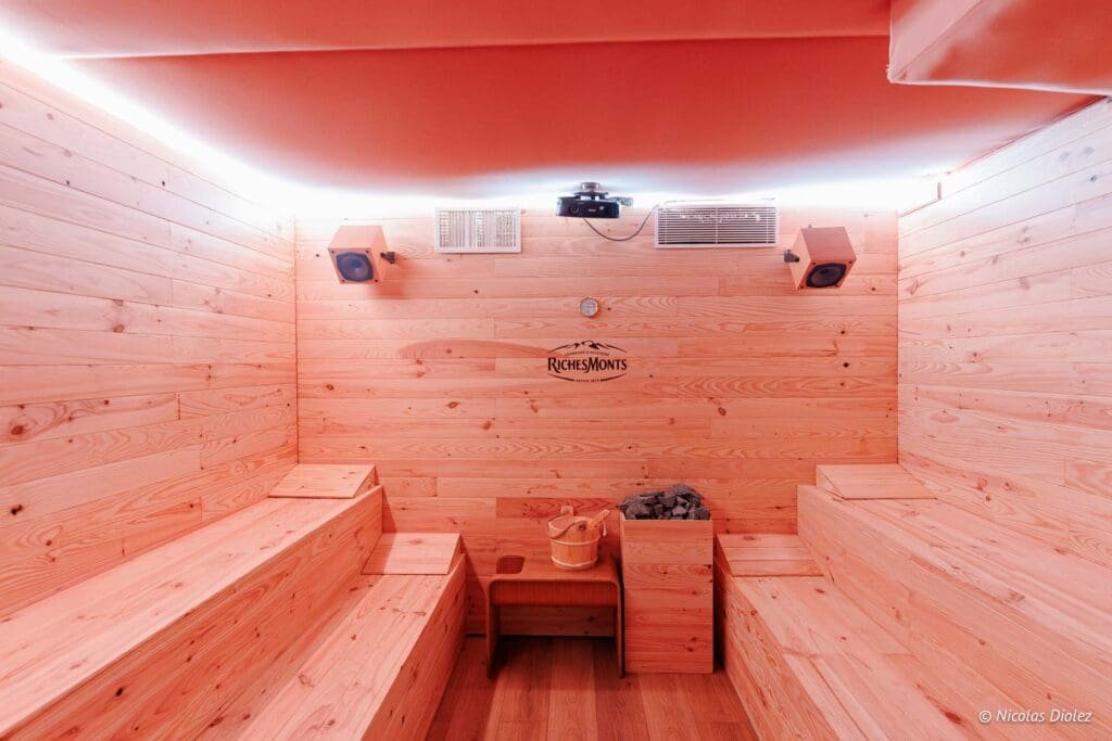 Intérieur de sauna en bois clair avec logo Richesmonts, bancs et seau.