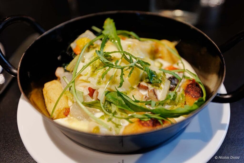 Plat gratiné aux légumes, fromage et roquette servi dans une petite poêle noire.