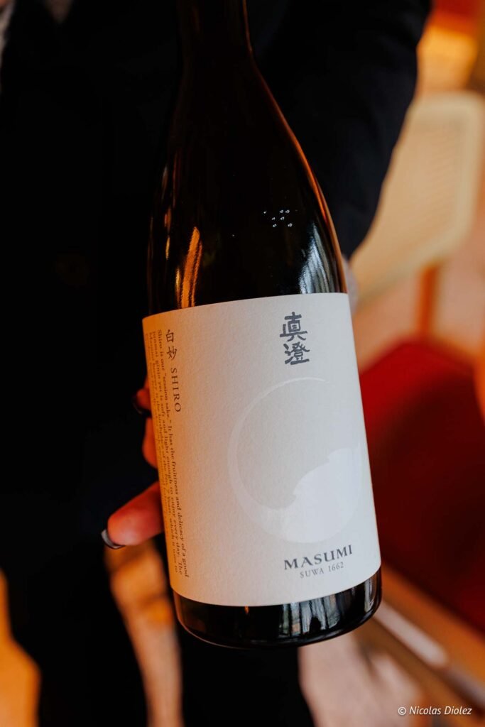 Bouteille de saké Masumi Suwa 1662, étiquette Shiro tenue à la main.