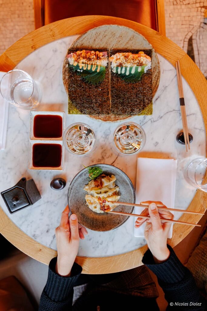 Person mangeant des gyozas avec des baguettes, table marbre Vesper Paris.