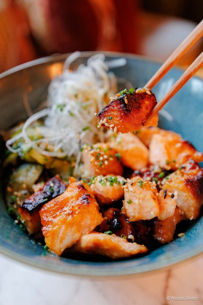 Morceaux de saumon caramélisé aux sésames avec vermicelles servis aux baguettes.