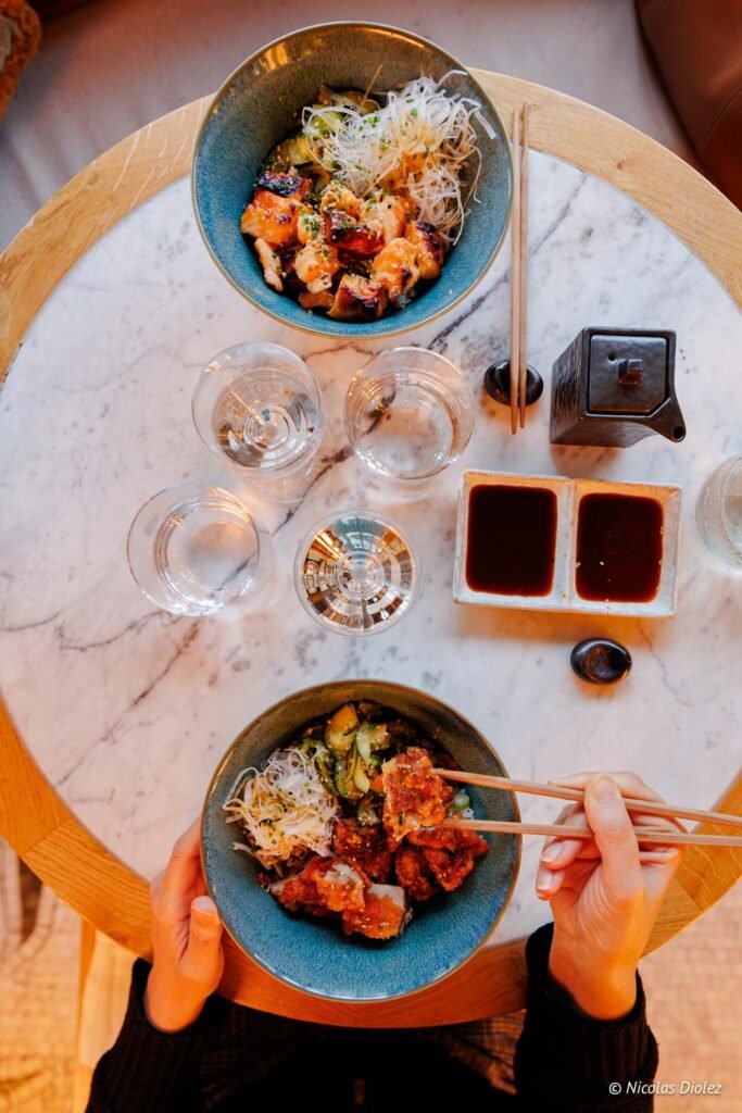 Repas japonais avec bol de poulet frit, nouilles et légumes, vue plongeante.