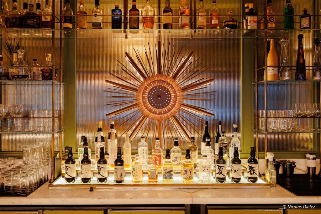Bar Vesper Paris, rayons de soleil décoratifs, étagères de bouteilles de spiritueux et saké.
