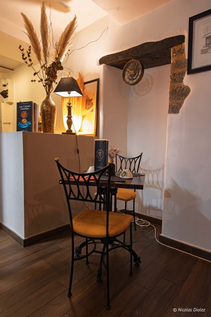 Coin salon avec chaises en fer forgé, horloge ancienne et fleurs séchées.