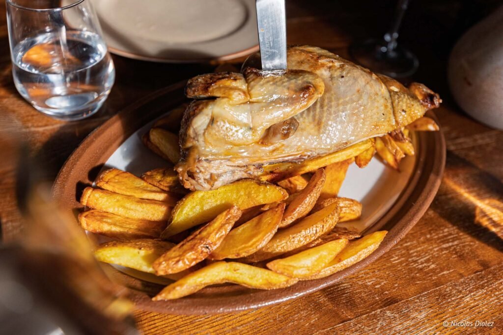 Poulet rôti sur quartier de pommes de terre frites, couteau planté.