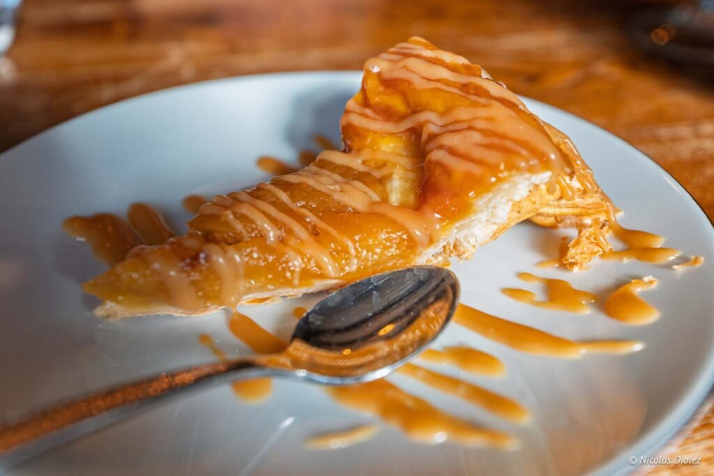 Tranche de tarte aux pommes nappée de caramel sur une assiette blanche.