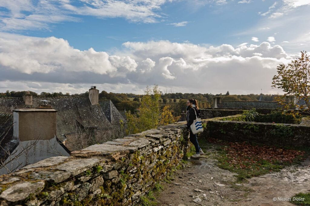 Vue femme contemplant le paysage de Rochefort-en-Terre depuis un mur de pierre.