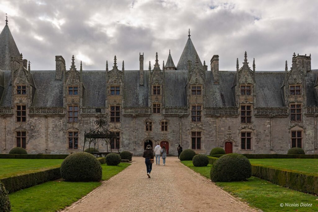 Château de Josselin entrée avec allée et jardins sous un ciel nuageux.