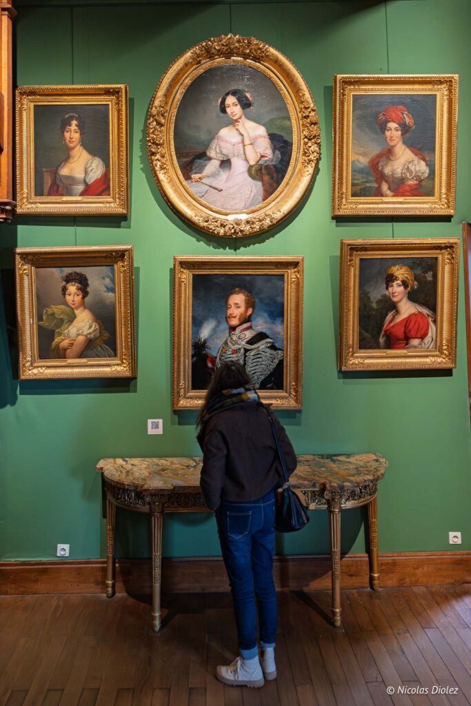 Visiteur admirant des portraits du Château de Josselin sur mur vert.