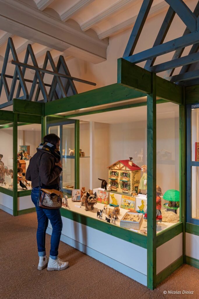 Visiteur observant des jouets anciens, dont une maison de poupée, dans une vitrine au Château de Josselin.