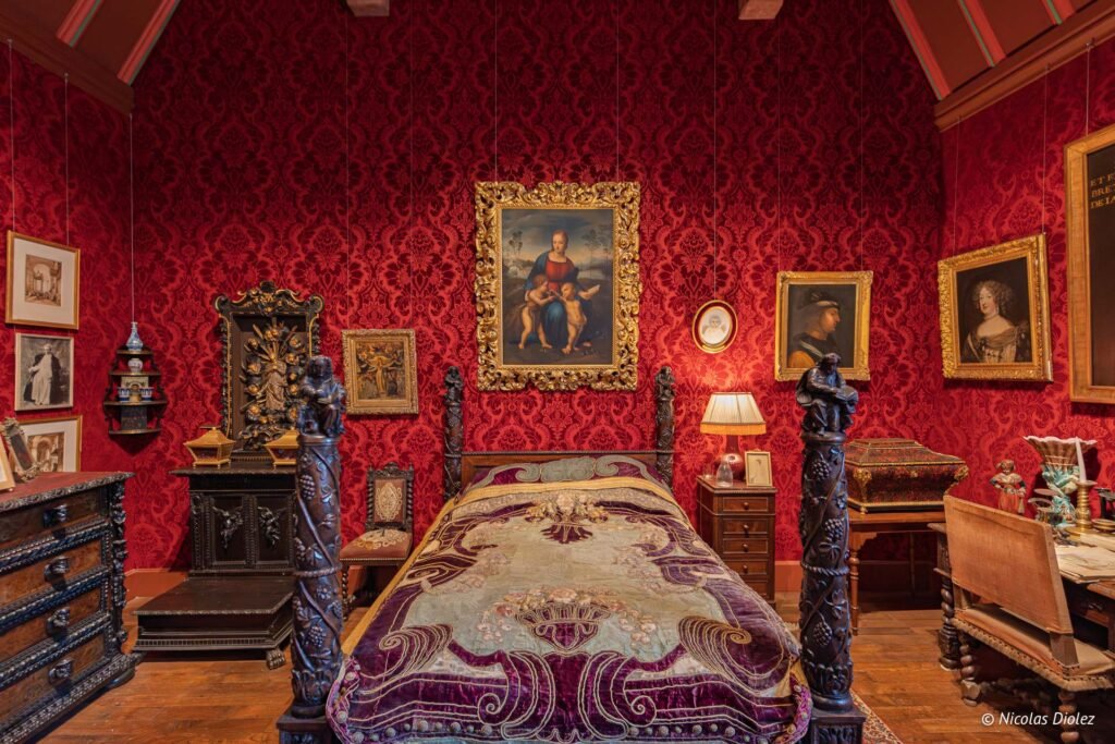 Chambre historique du Château de Josselin avec tentures rouges et lit à baldaquin sculpté.