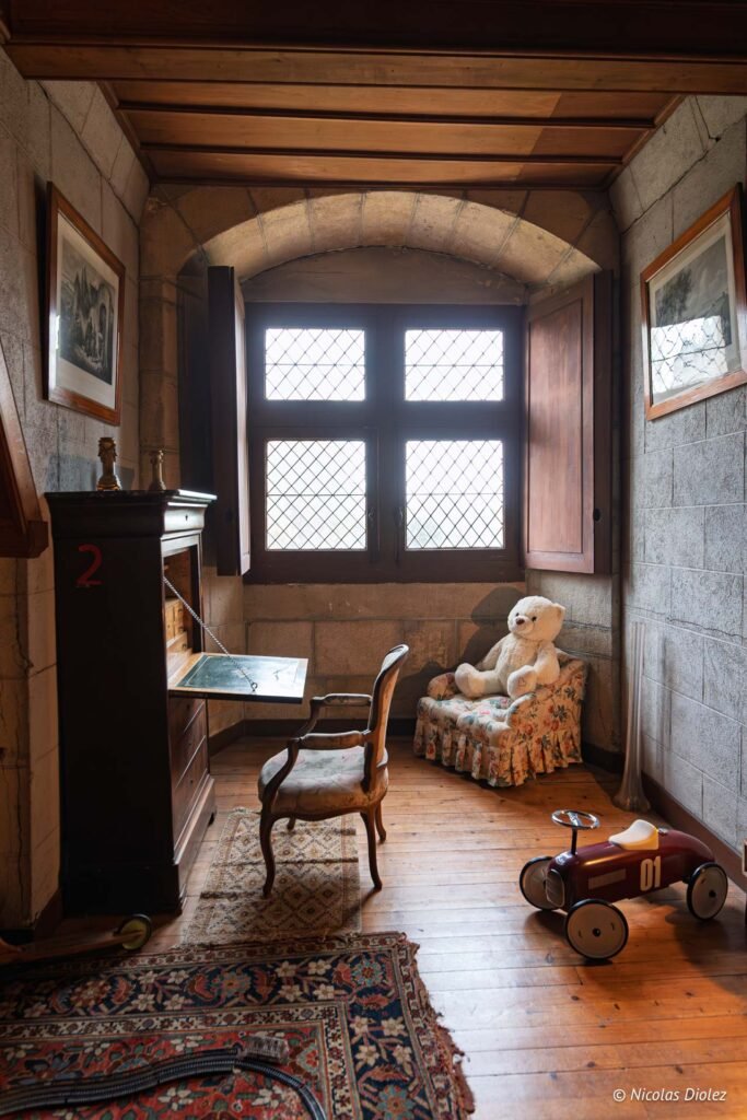 Intérieur d'une pièce du Château de Josselin, enfant avec ours en peluche, secrétaire et voiture à pédales.
