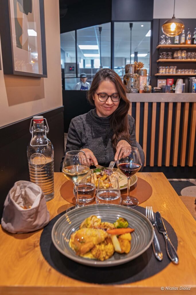 Femme mangeant un plat au restaurant Chez Simon Josselin, verres de vin.