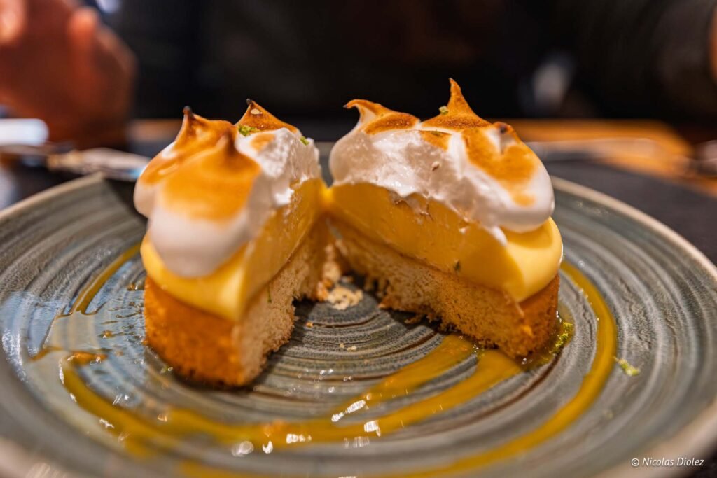 Tarte au citron meringuée coupée en deux, décorée de sauce jaune sur assiette.