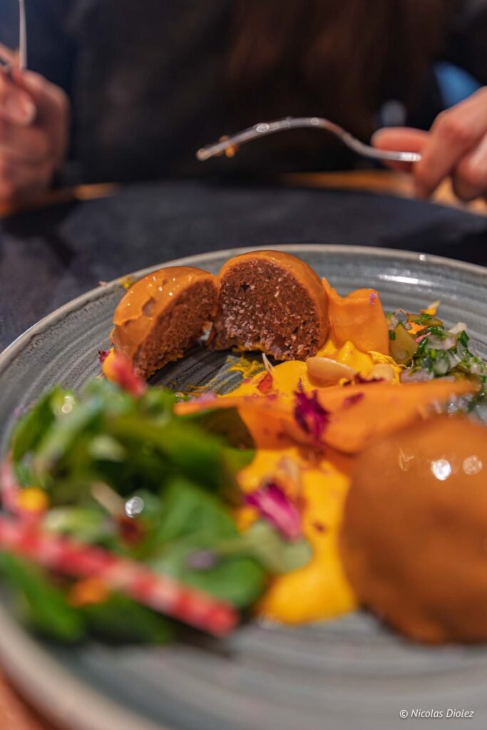 Gros plan sur plat gastronomique coupé, sauce orange, légumes, Chez Simon Josselin.