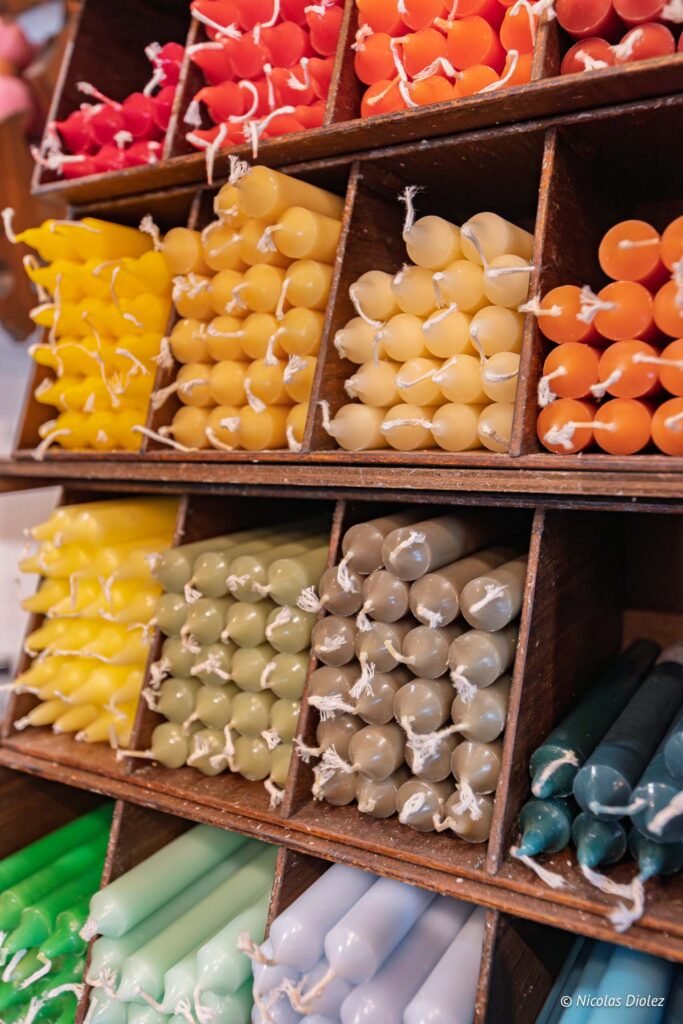 Bougies colorées empilées dans des casiers en bois chez Commerces Rochefort-en-Terre.