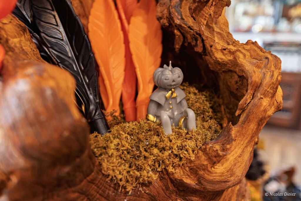 Figurine citrouille d'Halloween grise dans une décoration en bois avec mousse et feuilles oranges.